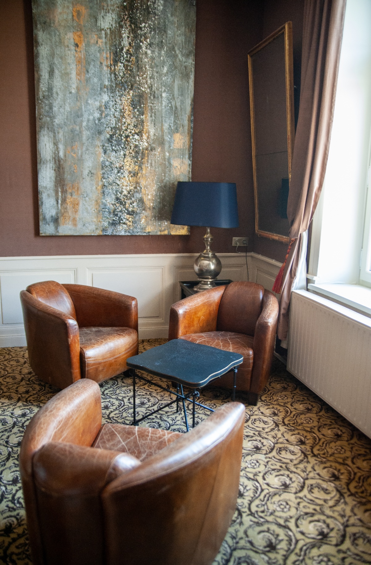 Petit salon aux murs prune avec fauteuils club en cuir patiné et toile contemporaine