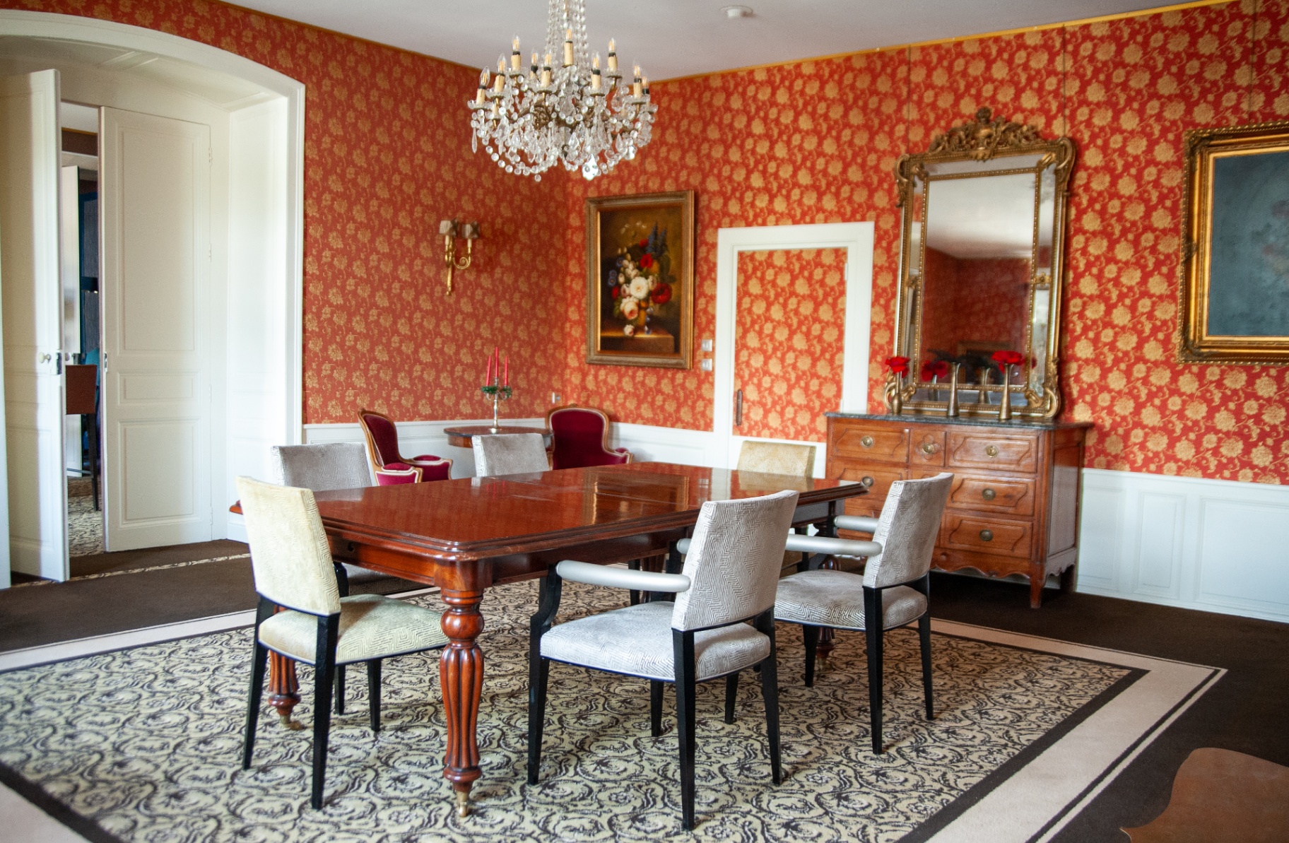 Salle à manger aux papiers peints rouge et or, lustre en cristal et table d'apparat