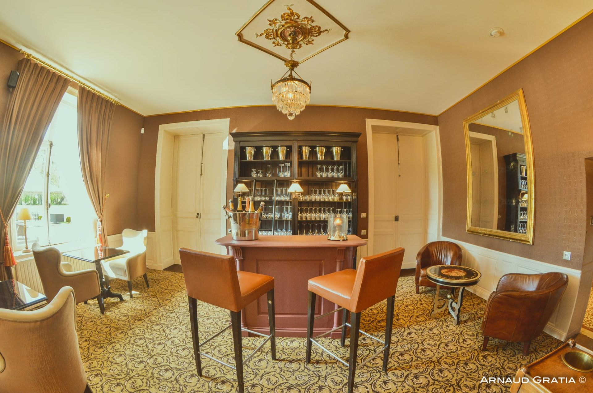 Salon bar du château avec comptoir rose poudré, tabourets de bar en cuir orange et fauteuils club