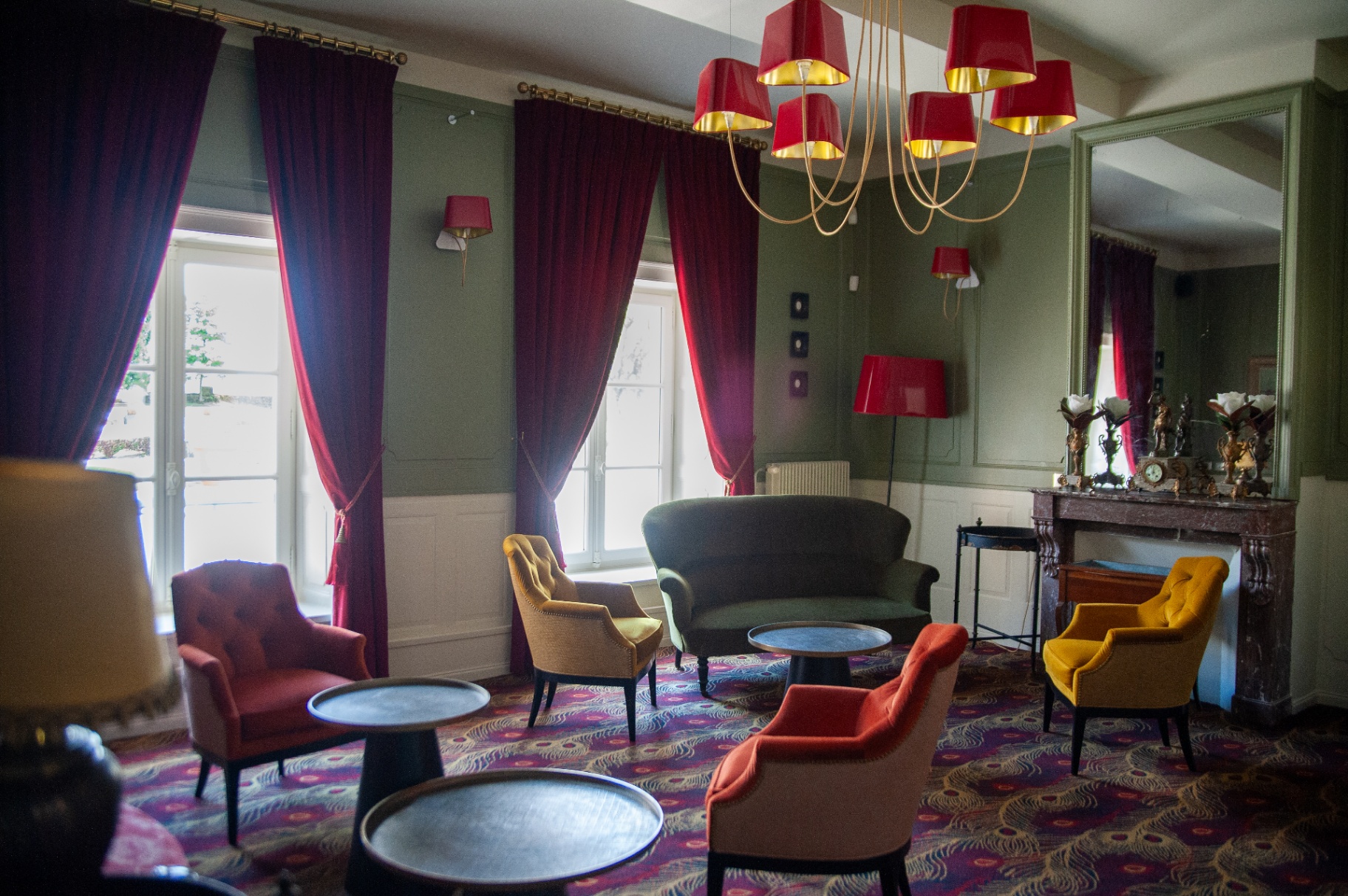 Grand salon vert avec rideaux de velours grenat, fauteuils colorés et cheminée en marbre