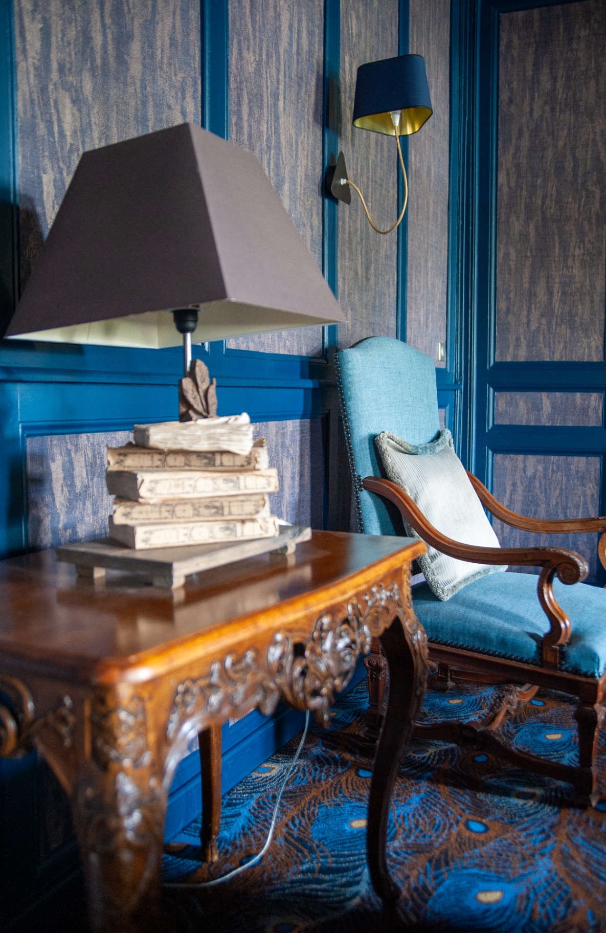 Coin lecture aux boiseries bleues avec console sculptée, fauteuil bleu et livres anciens