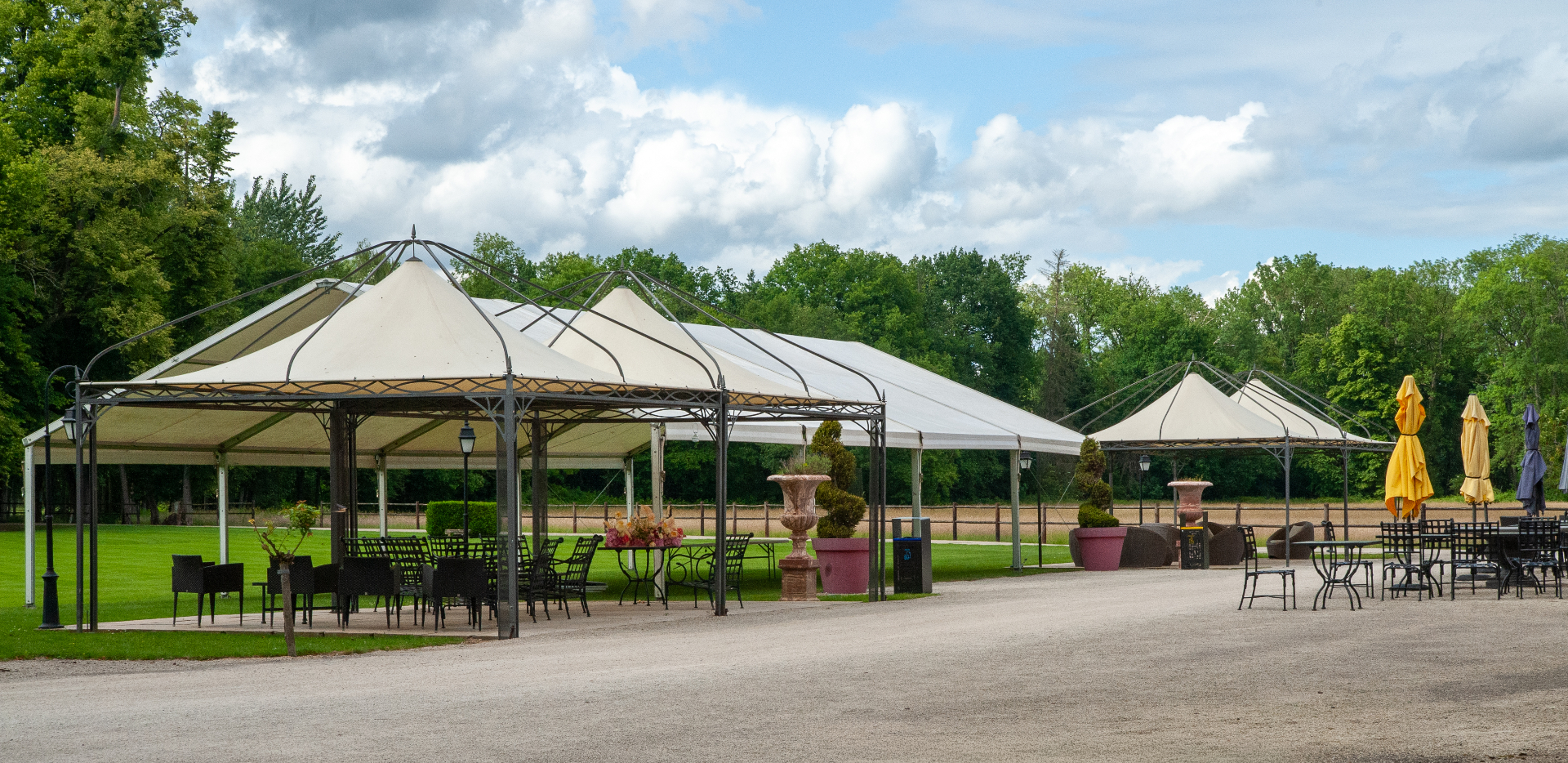 Terrasses du château avec tonnelles, mobilier en fer forgé et vue sur le parc