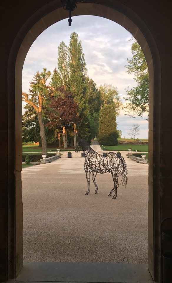 Sculpture de cheval en fil de fer encadrée par l'arche de pierre du château
