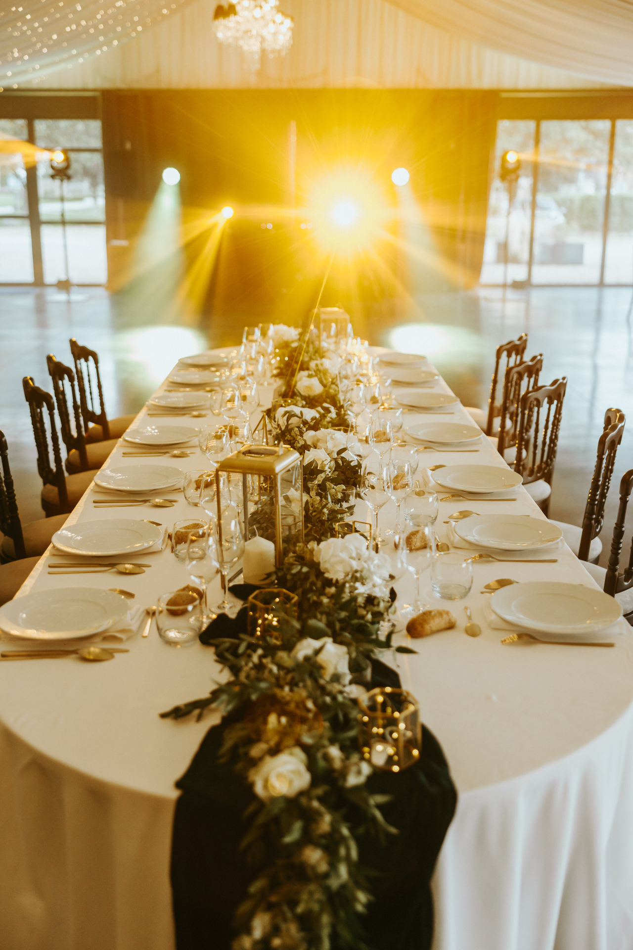 Grande table dressée dans le salon champêtre avec guirlande florale et éclairages dorés